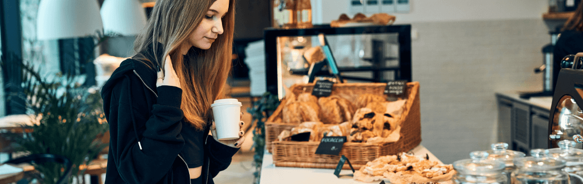 woman holding coffee looking at pastries on counter