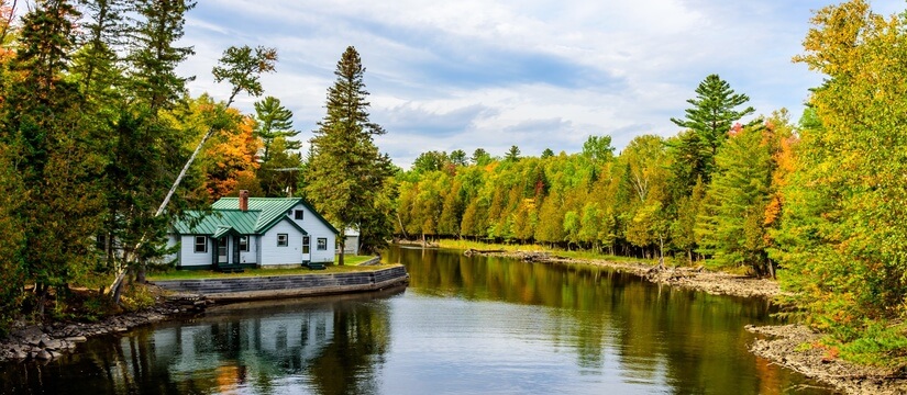 House and reflection on a river in Maine surrounded by autumn foliage