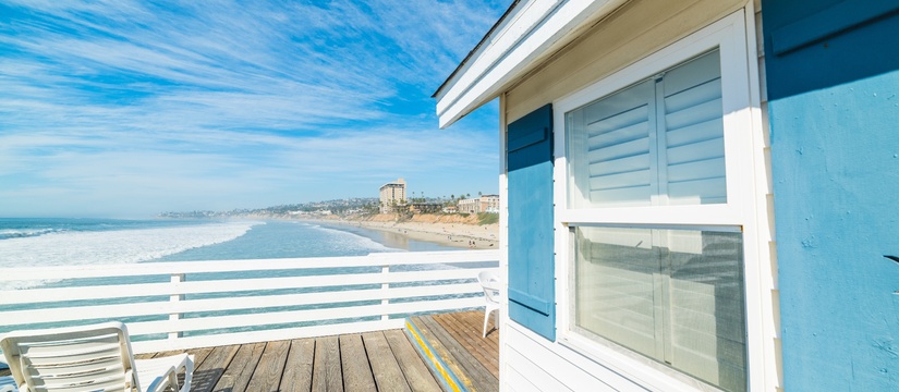 White house with blue shutters on California beach with blue ocean and sky.