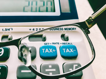 Close-up of reading glasses held next to tax keys on calculator
