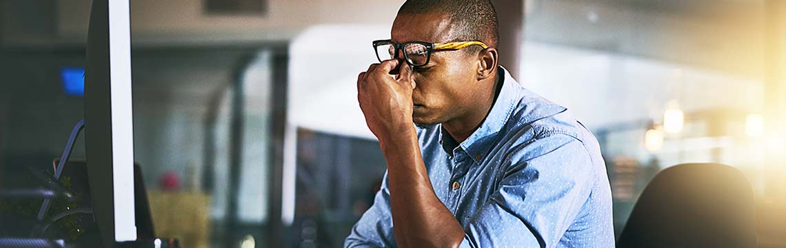 Businessperson sitting at desk rubbing forehead.