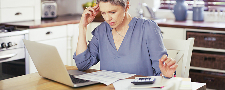 Woman doing taxes at kitchen table with calculator and laptop