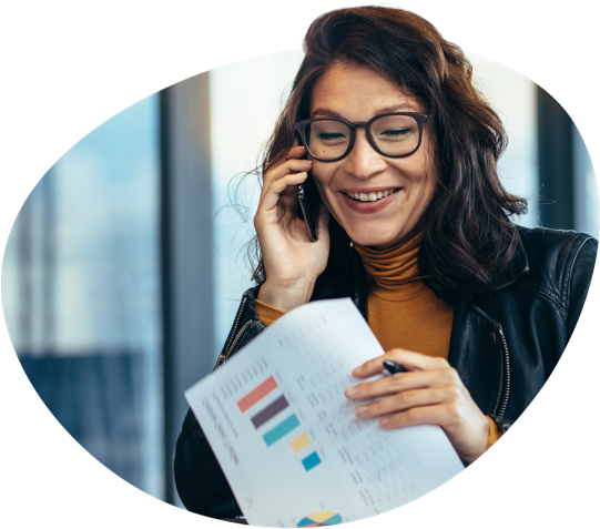 Person holding a document with colourful charts and graphs, speaking on a phone in a modern office setting.