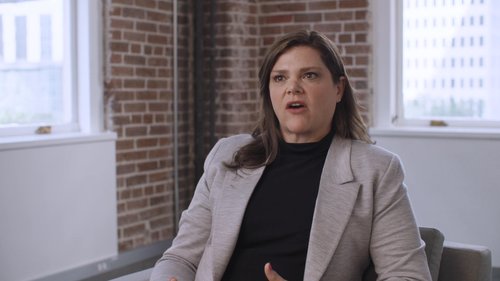 A professional woman in a blazer speaks in an office setting, featured in a Set Solutions customer story video.