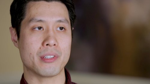 A person seated in a modern office with exposed brick walls and large windows.