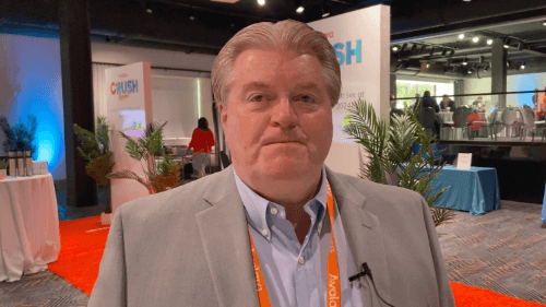 Two people in a meeting room with laptops open on a wooden table, discussing work.
