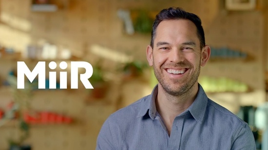 The MiiR logo displayed against a blurred background with colorful shelves and plants.