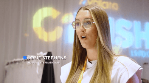 Two people in a meeting room with laptops open on a wooden table, discussing work.