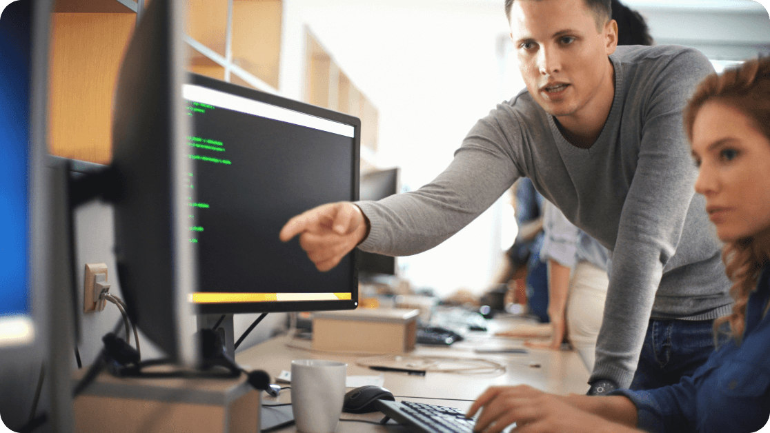 Two colleagues working together in a coding program at an office workstation.