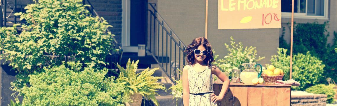 Lemonade stand with a girl in front of a house.