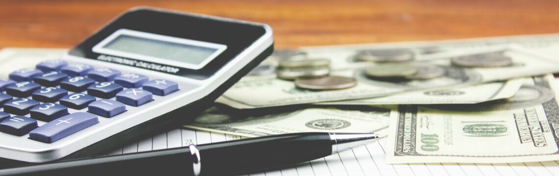 Calculator, pen, and money sitting on top of a pad of paper