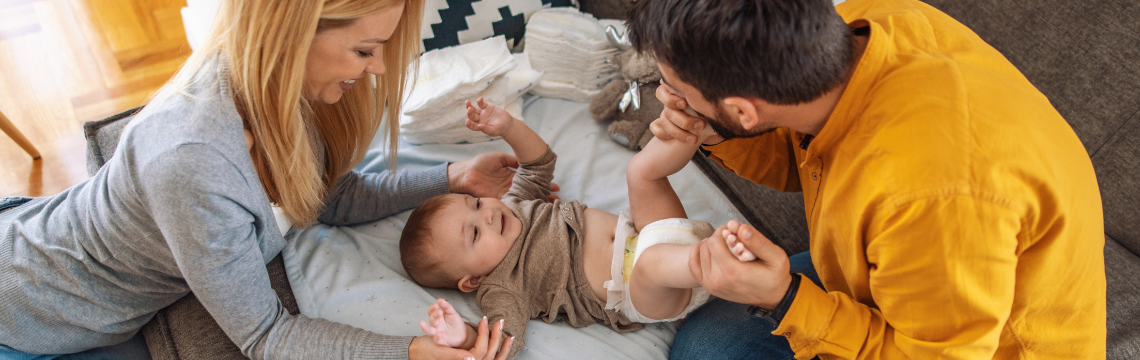 Parents putting a diaper on their baby. Two parents with their baby, who is wearing a diaper.